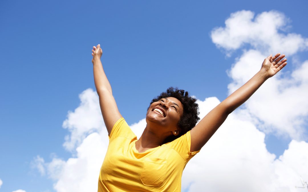 Cheerful young woman with hands raised towards sky