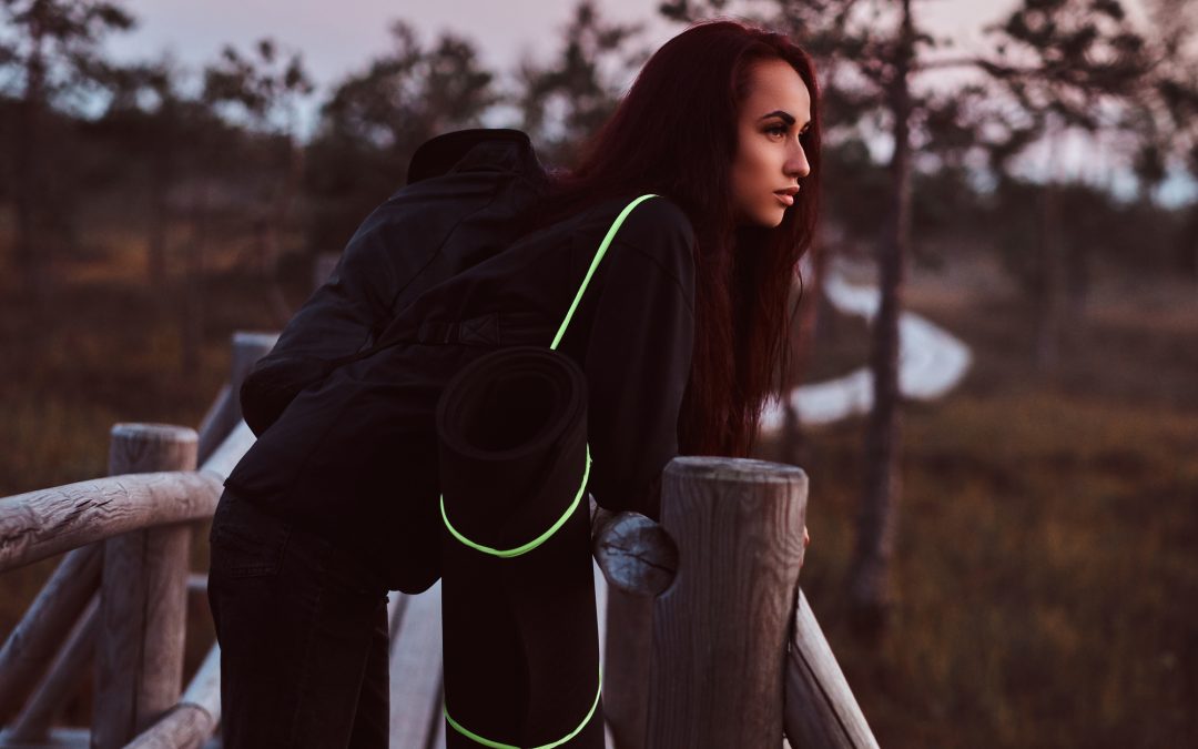 Woman in a black hoodie and jeans leaning on a wooden fence in a beautiful autumn meadow at sunset.