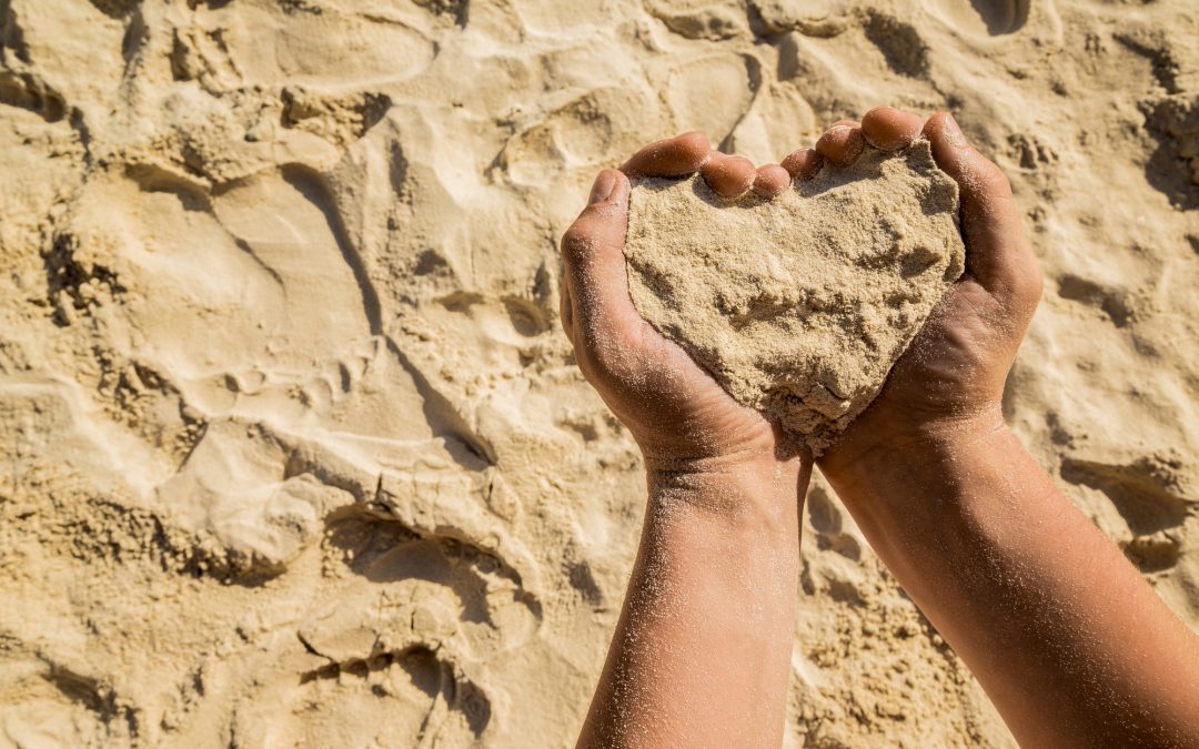 Heart from sand, a symbol in a hand.